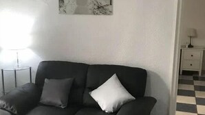 A black leather sofa with two pillows, a small side table, a lamp, and a checkered floor.