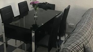 A compact room with a dining table, chairs, a small kitchen area, and a bed.