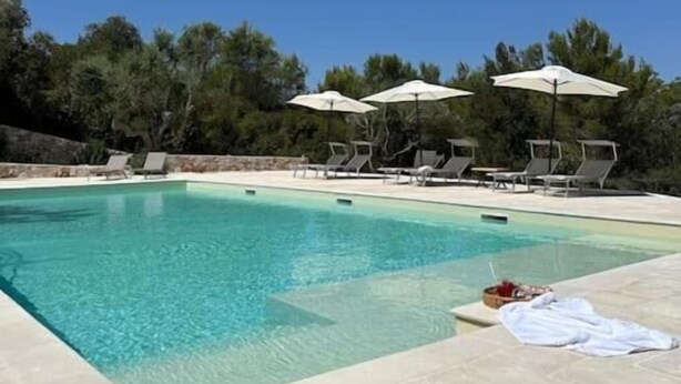 Une piscine à l’eau d’un bleu cristallin, entourée de chaises longues et de parasols, avec un décor de verdure en arrière-plan.