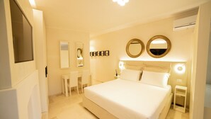 Une chambre à coucher avec un grand lit, des tables de chevet, un bureau, des chaises et deux miroirs fixés au mur.