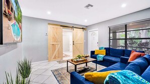 Una sala de estar moderna con un sofá azul, una mesita de centro y una puerta corrediza tipo granero que da a una zona de piscina.