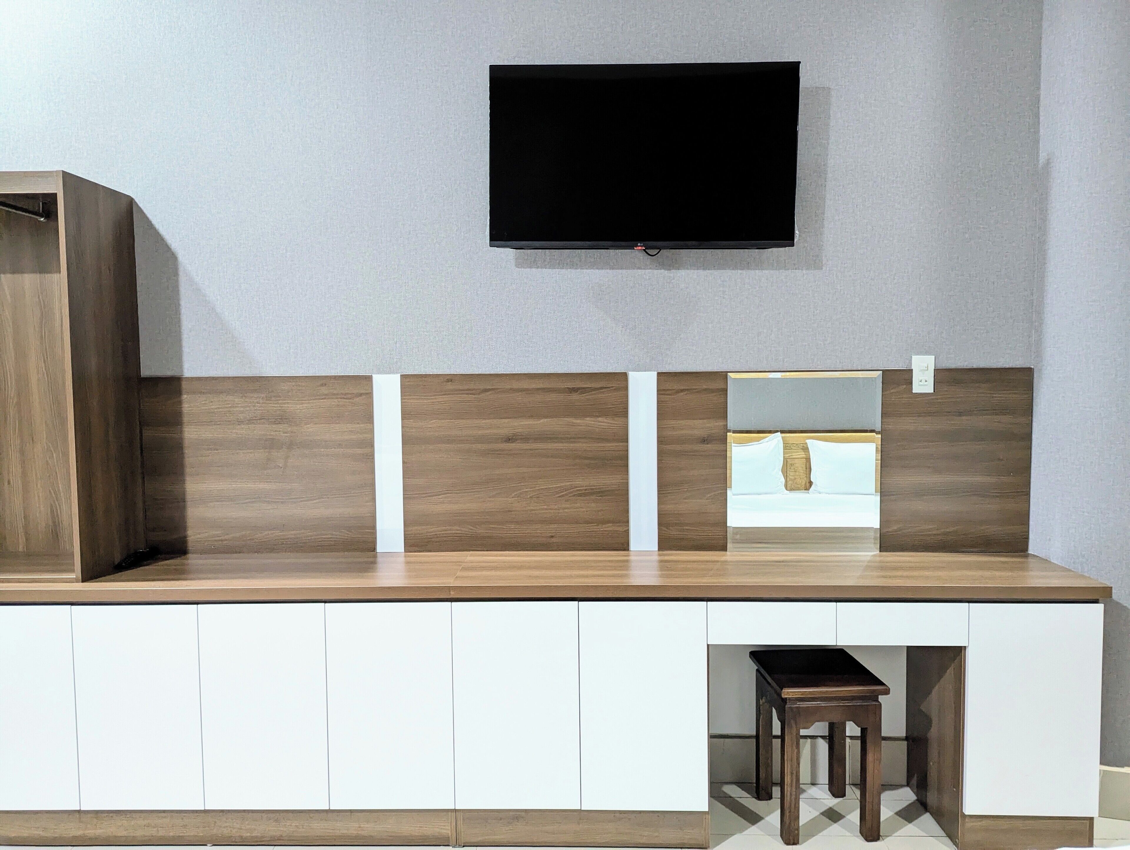A modern room with a wooden desk, a television mounted on the wall, and a small stool.