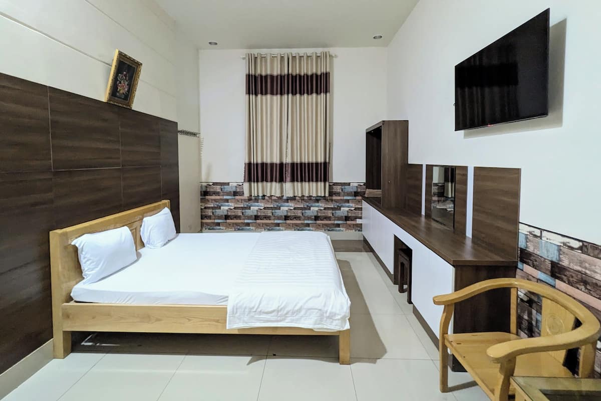 Quarto com cama de madeira, televisão fixada na parede e uma cadeira de madeira pequena.