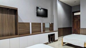 Moderni hotellihuone, jossa on suuri sänky, pienempi sänky, seinälle asennettu televisio ja puinen meikkipöytä peilillä.