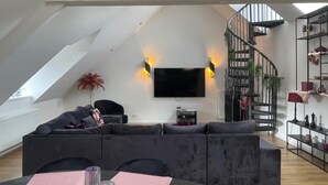 Ein modernes Loft mit hoher Decke, einem großen grauen Ecksofa, einem flachbildfernseher an der Wand und einer Wendeltreppe.