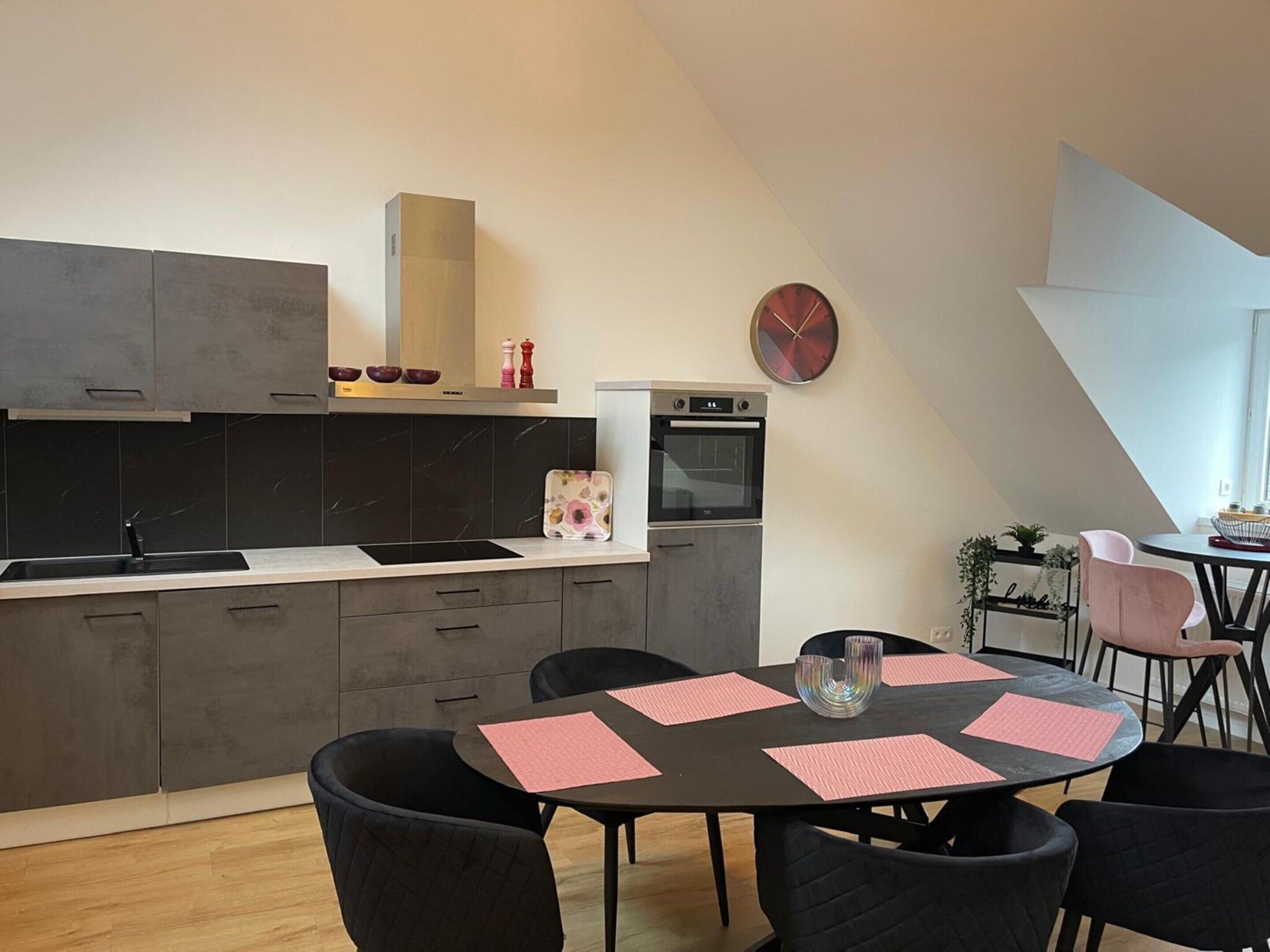 Een moderne keuken met donkere kastjes, een ingebouwde oven en een eethoek met een ronde tafel en stoelen.