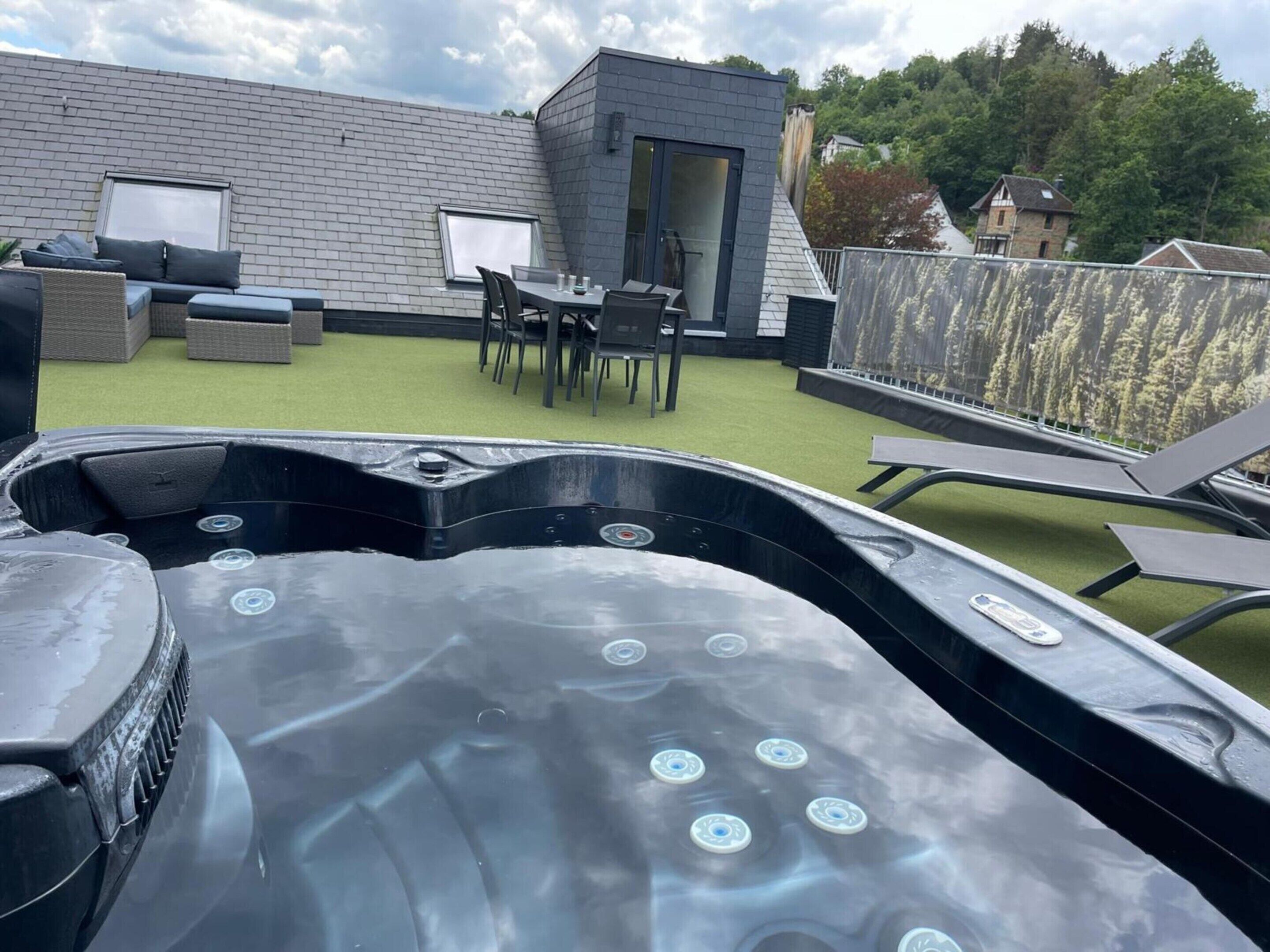 A rooftop patio with a hot tub, outdoor seating, and a small building.