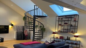 Ein modernes Wohnzimmer mit einem dunkelblauen Sofa, einer Wendeltreppe, einem Oberlicht und einem dekorativen Regal mit Keramik.