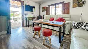 A modern living room with a wooden dining table, red stools, a white sofa, and a television mounted on the wall. - Farmhouse in the Picturesque Village of Frigiliana (Frigiliana)