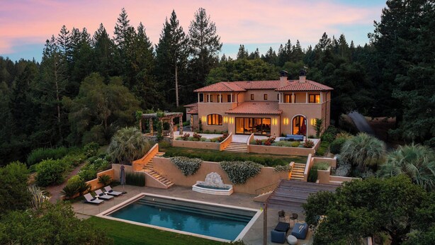 A two-story house with a swimming pool, surrounded by lush greenery and trees.