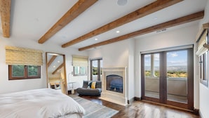 A bedroom with a bed, a fireplace, a balcony with a view, and wooden beams on the ceiling.