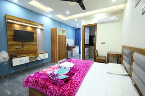 A bedroom with a bed, a TV mounted on the wall, a wardrobe, a desk, and a chair. - Radha krishna spiritual stay  (Vrindavan)
