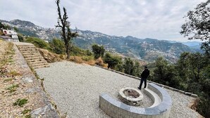 Een rond steenstructuur met een persoon erop, omgeven door een grindpad en een uitzicht op een glooiend landschap.
