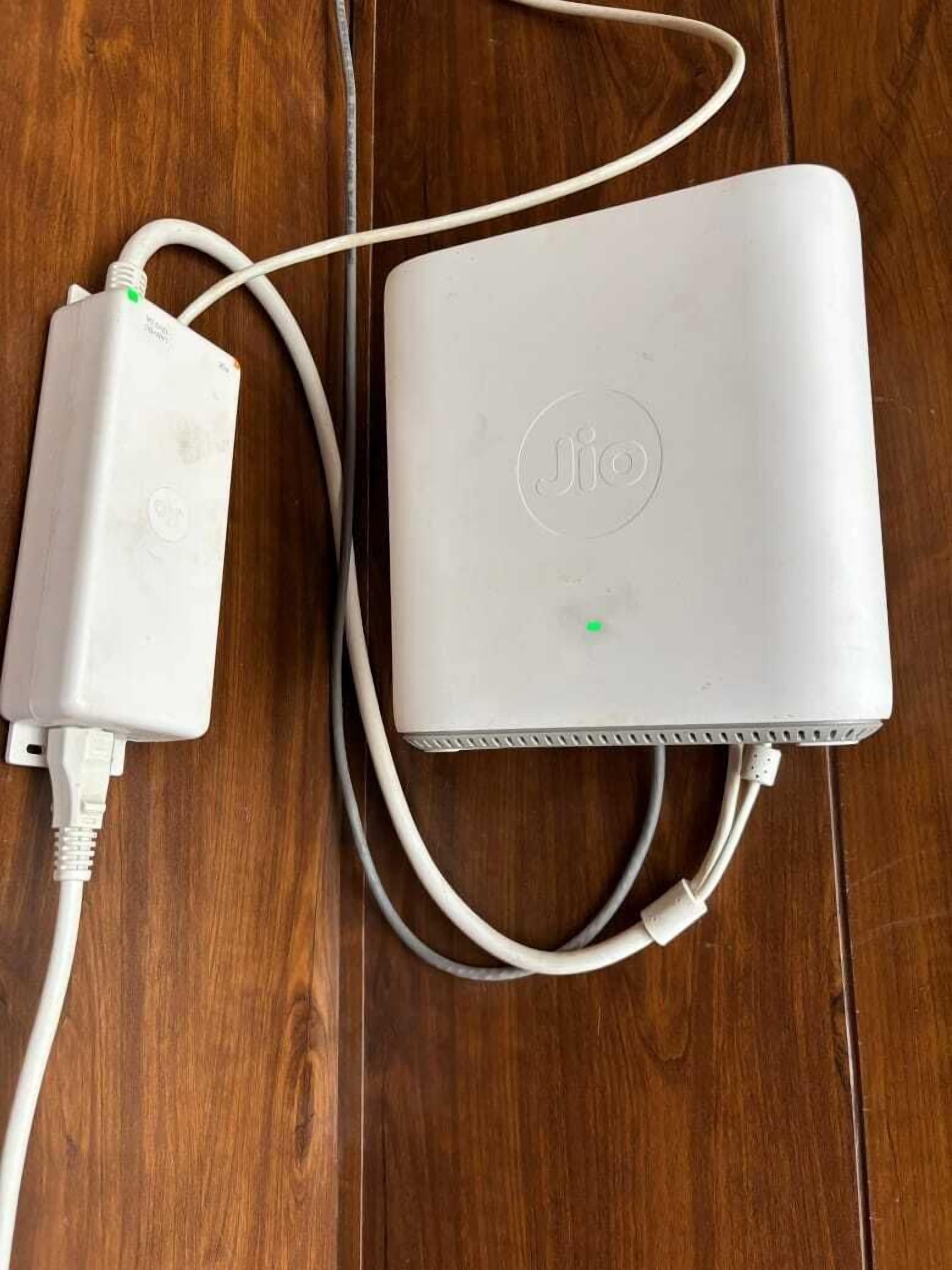 En hvid Jio-modem tilsluttet en strømadapter på en træoverflade.