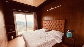 Een slaapkamer met een groot bed, houten wanden, uitzicht door een schuifdeur en een klein tafeltje met een radio.