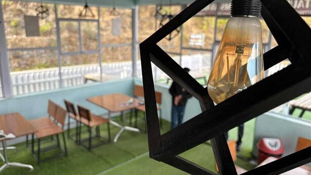 Een zithoek met tafels en stoelen, een hanglamp en een uitzicht door grote ramen.