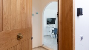 Puerta de madera que da a un cuarto con pared blanca, un televisor montado y una mesa pequeña con sillas.