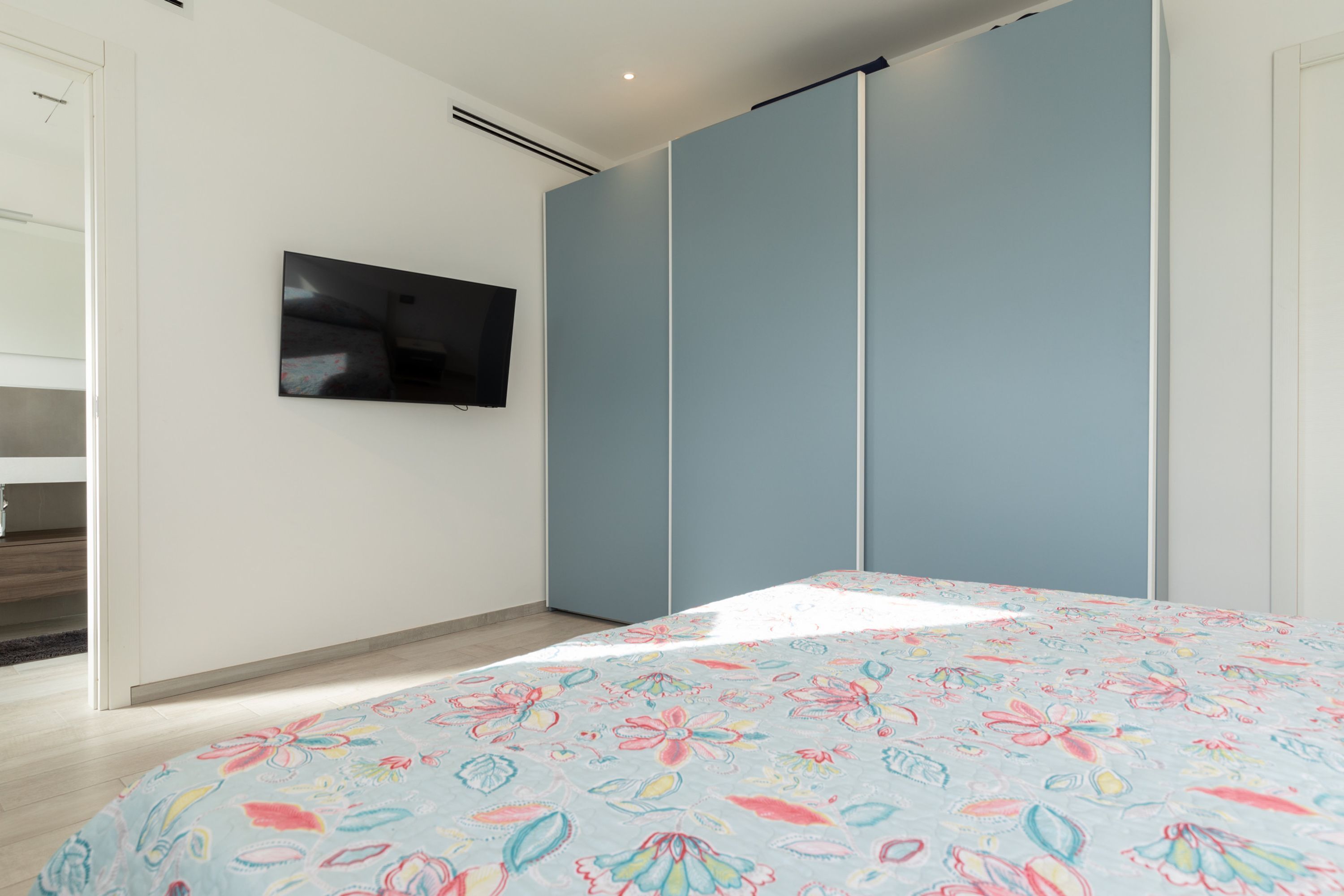Un dormitorio con cama, televisor en la pared y armario.