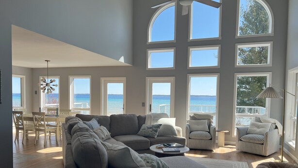 A spacious living room with a large sectional sofa, a dining area with a table and chairs, and multiple windows offering ocean views.