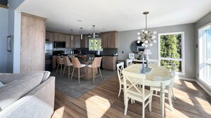 A modern kitchen with a central island, bar stools, and a dining area with a white table and chairs.