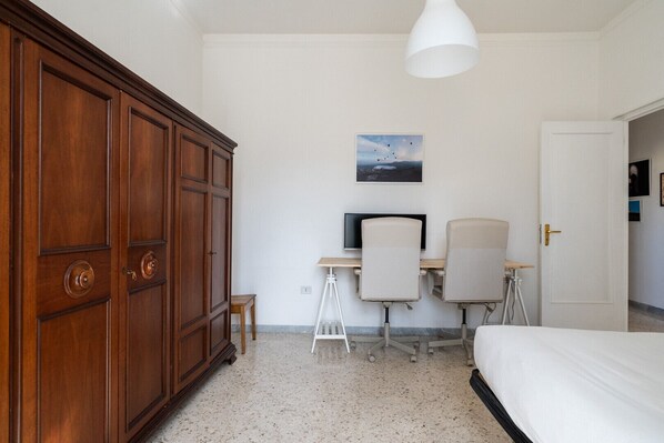 Ein Schlafzimmer mit großem Holzschrank, Schreibtisch mit zwei Stühlen, Bett und Deckenleuchte.