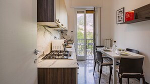 A compact kitchen with a gas stove, a dining table with chairs, and a view through a glass door to an outdoor balcony.