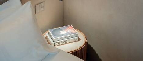Un lit bien fait, avec un oreiller, une table de chevet sur laquelle reposent deux livres et un luminaire fixé au mur.