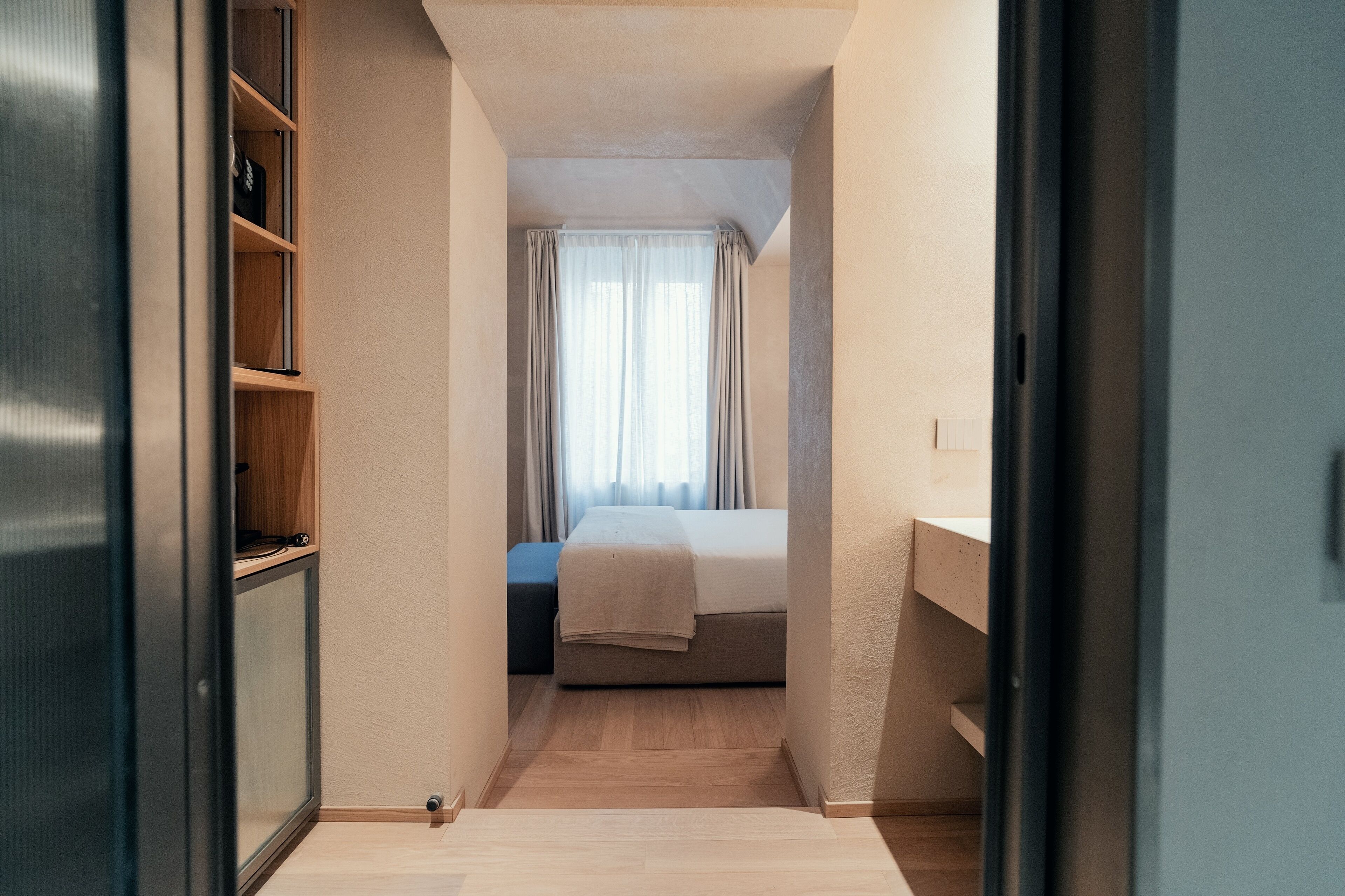 Un couloir étroit mène à une chambre à coucher qui contient un lit, une table de chevet et une armoire.