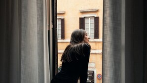 A person standing by a window with a view of a building with brown shutters. - VELVET GREY BOUTIQUE HOTEL ROMA (Rome)