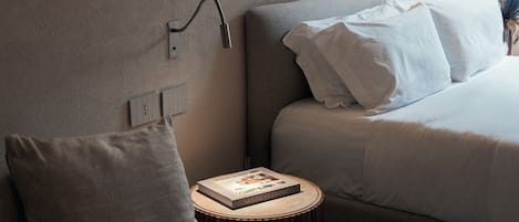 A hotel room with two beds, a bedside table with a book, and a wall-mounted lamp.