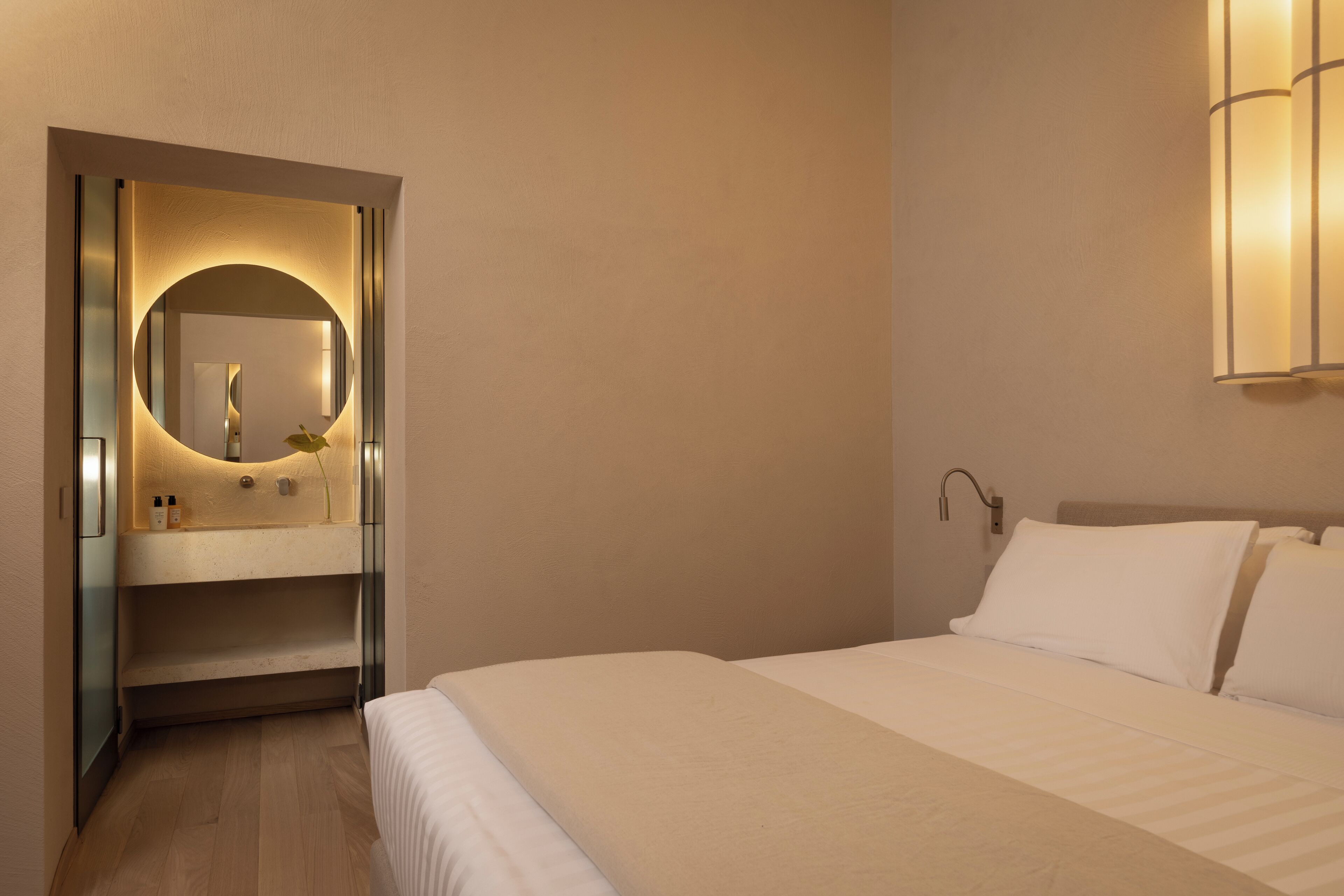 Une chambre d’hôtel comprenant un lit, une table de chevet, un miroir et un luminaire fixé au mur.