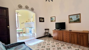 Ένα σαλόνι με τηλεόραση, ένα ξύλινο έπιπλο και μια τραπεζαρία στο βάθος.