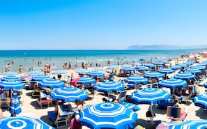 A beach with numerous blue umbrellas and sun loungers, indicating a beachside resort setting. - Casa De Gasperi in Castellammare del Golfo (Castellammare del Golfo)