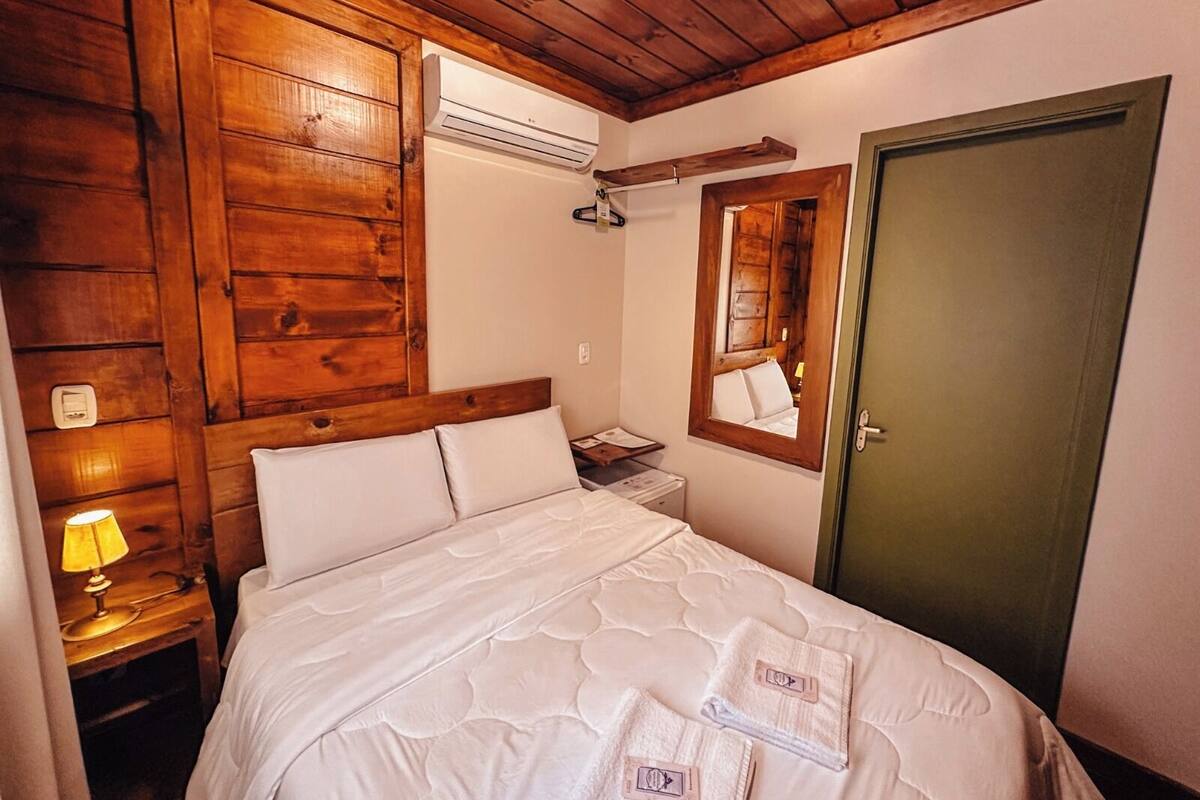 A bedroom with wooden paneling, a bed with white bedding, a bedside lamp, a mirror, and a door.