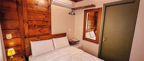 A bedroom with wooden paneling, a bed with white bedding, a bedside lamp, a mirror, and a door.