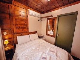 Un dormitorio con paneles de madera, una cama con ropa blanca, una lámpara de noche, un espejo y una puerta.