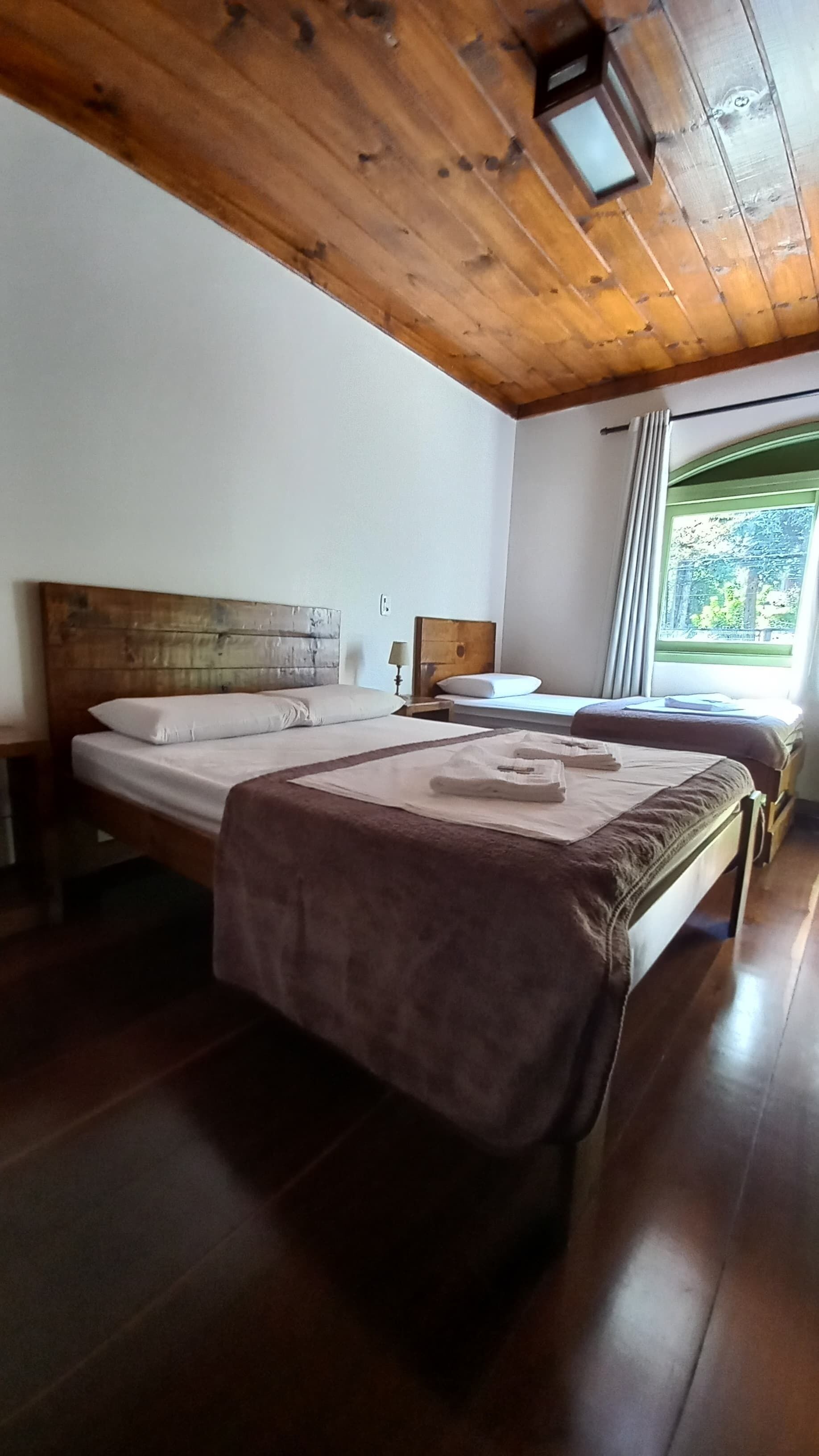 A bedroom with two beds, wooden ceiling, and a window with curtains.