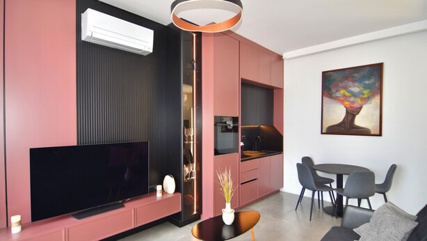 Una sala de estar moderna con un televisor de pantalla plana, un comedor con mesa y sillas, y una cocina con pileta y alacenas.