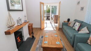 A cozy living room with a fireplace, a green sofa, a wooden coffee table, and a view through an open door to an outdoor area. - Arfryn (Haverfordwest)