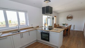 A modern kitchen with white cabinets, a built-in oven, and a large window. - Arfryn (Haverfordwest)
