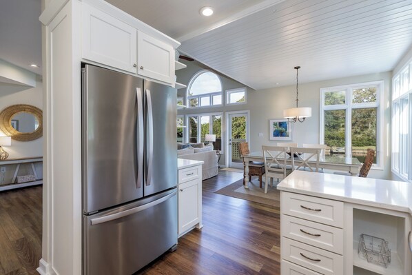 A modern kitchen with white cabinetry, a stainless steel refrigerator, and a dining area with a table and chairs.