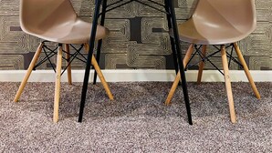 Un rincón de comedor con papel tapiz estampado, dos sillas, una mesa y una pequeña planta.