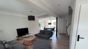 A modern living room with a flat-screen TV, grey sofas, a coffee table, and a dining area in the background. - House in Narbonne, ideal for Les Grands Buffets, with swimming pool and air-conditioning (Narbonne)