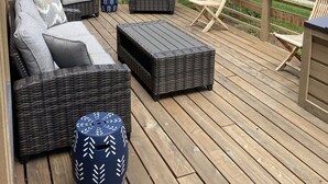 A deck with wicker furniture, including sofas and a coffee table, surrounded by a wooden railing.