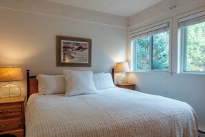 Un dormitorio con una cama, dos mesitas de noche, una ventana y un cuadro en la pared.