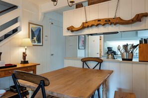 Un comedor con mesa y sillas de madera, una cocina al fondo y una escalera con un cuadro enmarcado en la pared.