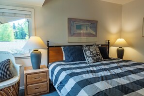A bedroom with a bed, two bedside lamps, a nightstand with a lamp, a chair, and a painting on the wall.