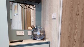 Una habitación pequeña con un armario de madera, un espejo, un ventilador y un televisor montado en la pared.