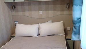Una cama con una colcha a rayas, dos almohadas blancas y un cabecero con armarios integrados.