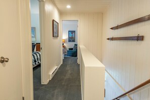 A narrow hallway with a carpeted floor, a bed with striped bedding, a framed picture on the wall, and a poster. - Remodeled 3BR Creekside Condo Sun Valley (Sun Valley)
